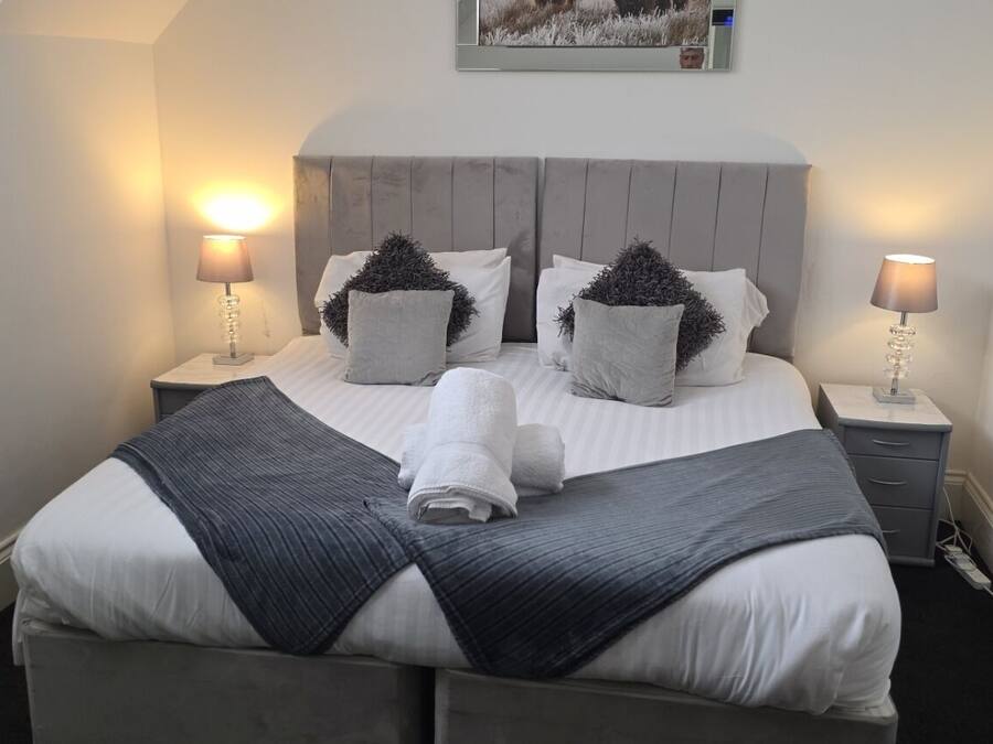 A neatly made bed with a grey headboard, two bedside lamps, and a framed picture on the wall.