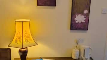 A hotel room with a bedside table, a lamp, a coffee maker, and two wall-mounted paintings.