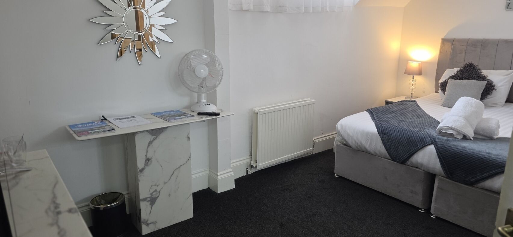 Habitación de hotel con cama, mesita de noche, lámpara y un ventilador en la pared.