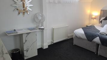 Habitación de hotel con cama, mesita de noche, lámpara y un ventilador en la pared.