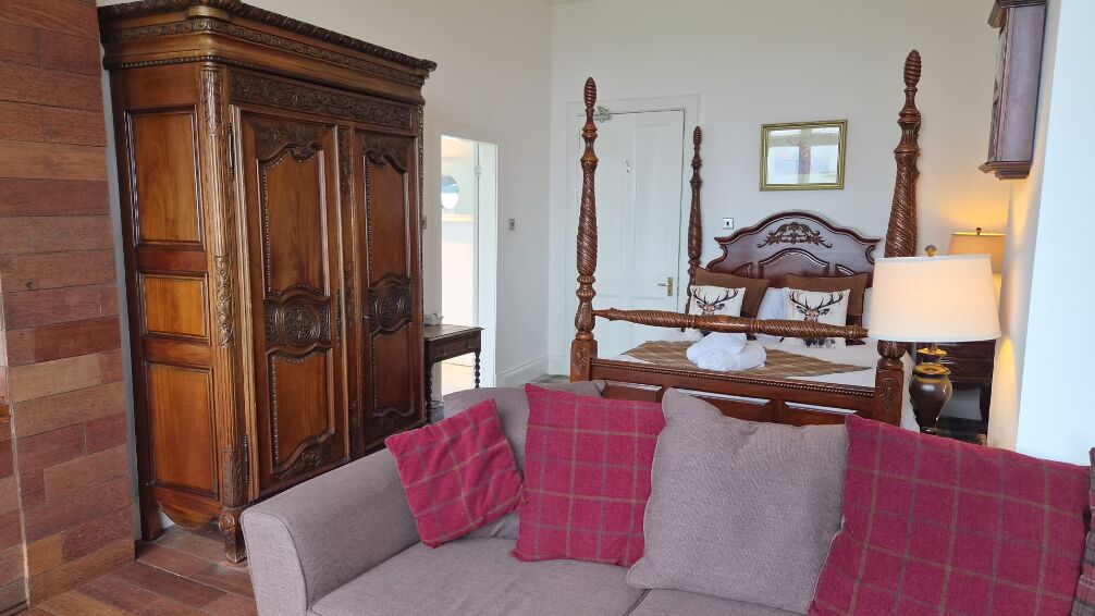 Een slaapkamer met een hemelbed, een houten garderobe en een grijze bank met geruite kussens.
