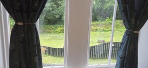 A window with curtains, a view of a garden, and a wooden fence. - Royal Marine Hotel (Dunoon)