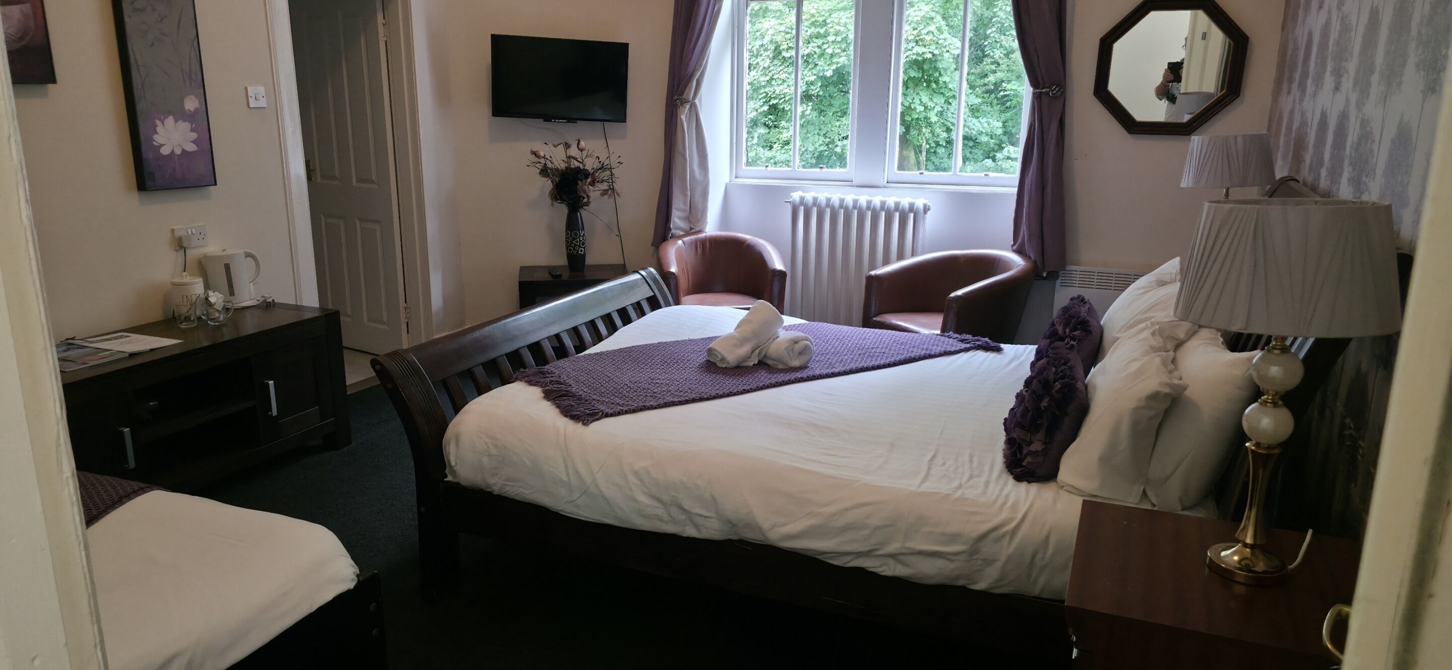 A hotel room with a bed, a desk, a chair, a TV, and a window with a view of trees.