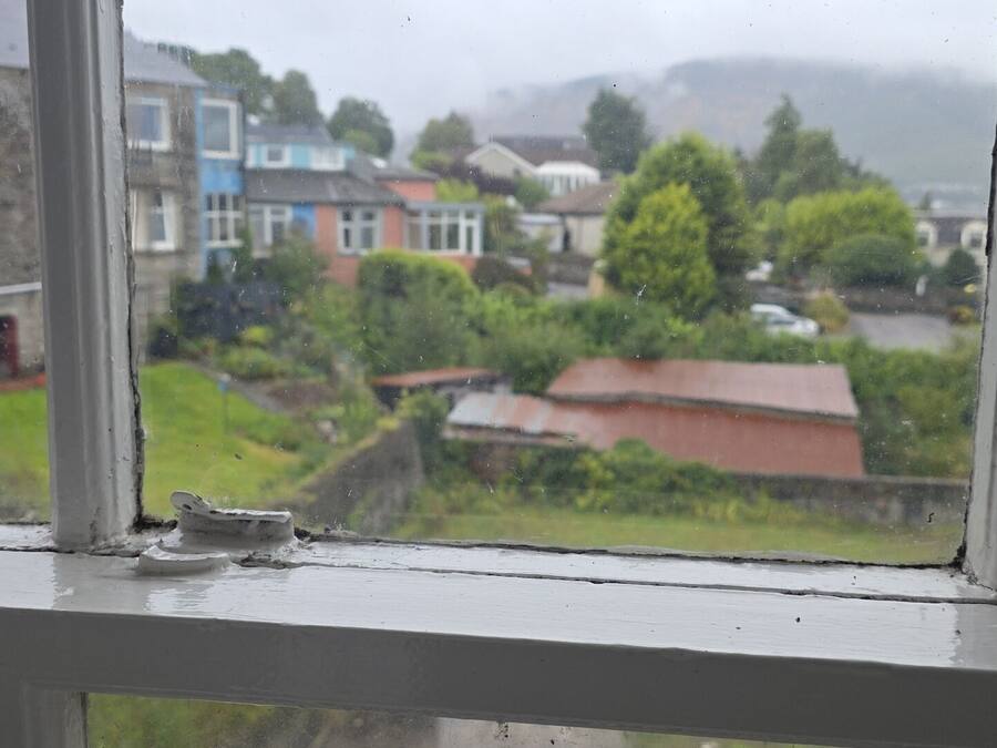 A view through a window with a white frame, overlooking a residential area with houses and greenery.
