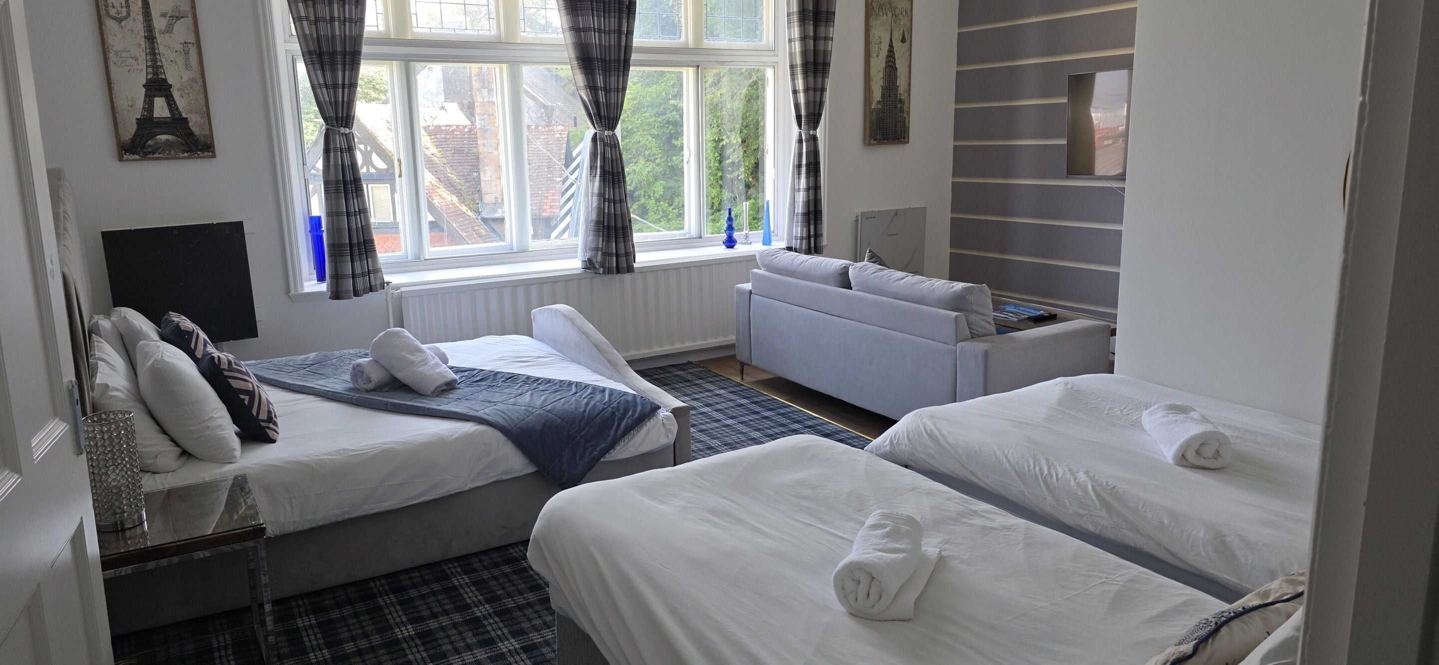 A hotel room with two beds, a sofa, a window with curtains, and a wall with a picture.