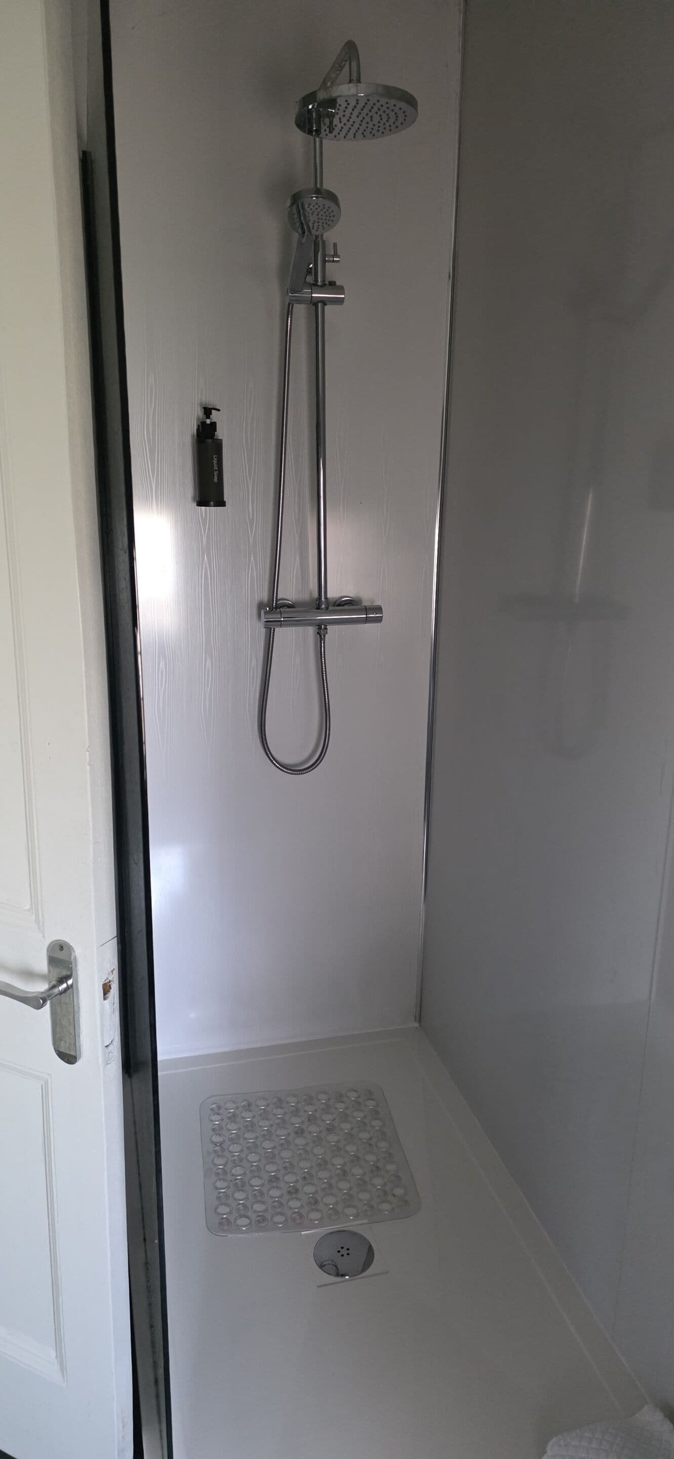 A shower enclosure with a handheld showerhead, a rain showerhead, and a handheld shower attachment.