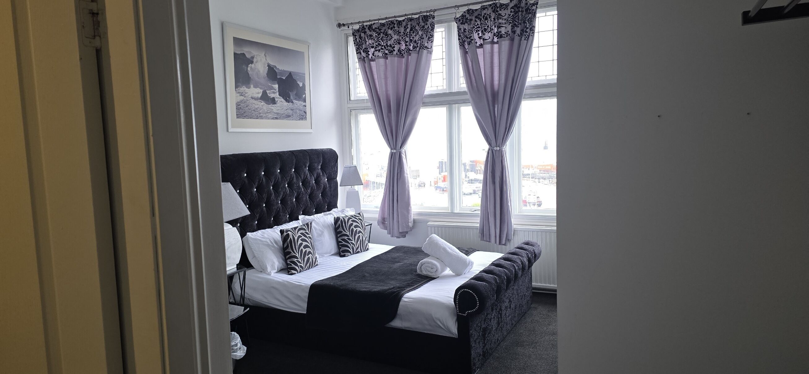Un dormitorio con cama, cabecera, ventana con cortinas e imagen colgada en la pared.