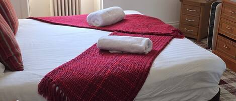 Quarto de hotel com cama, radiador, janela com cortinas, um quadro na parede e carpete estampado.