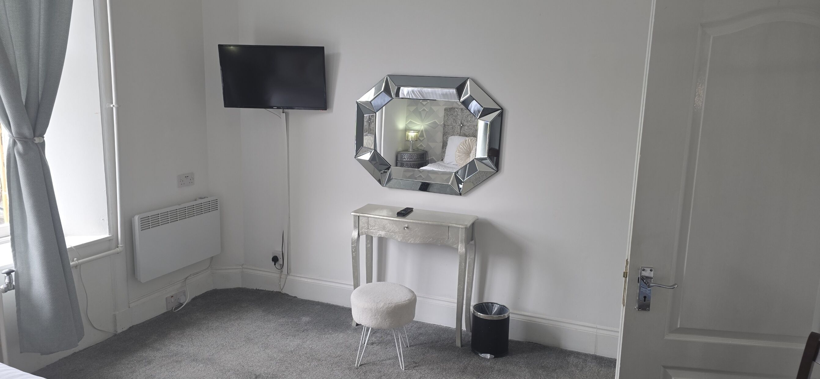 A room with a television, a mirror, a vanity table, a stool, and a door.
