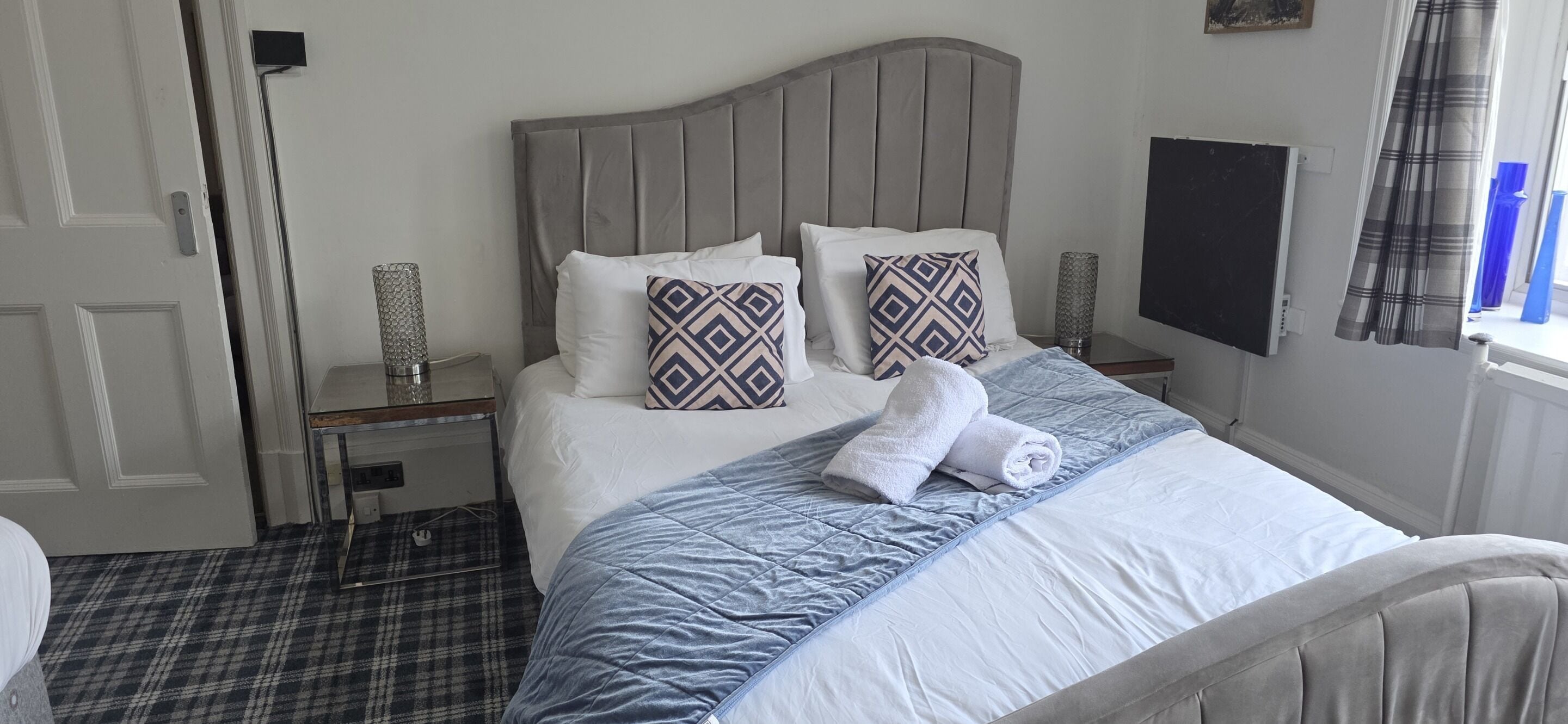 Una cama bien hecha con cabecera gris, ropa de cama blanca y almohadas estampadas.