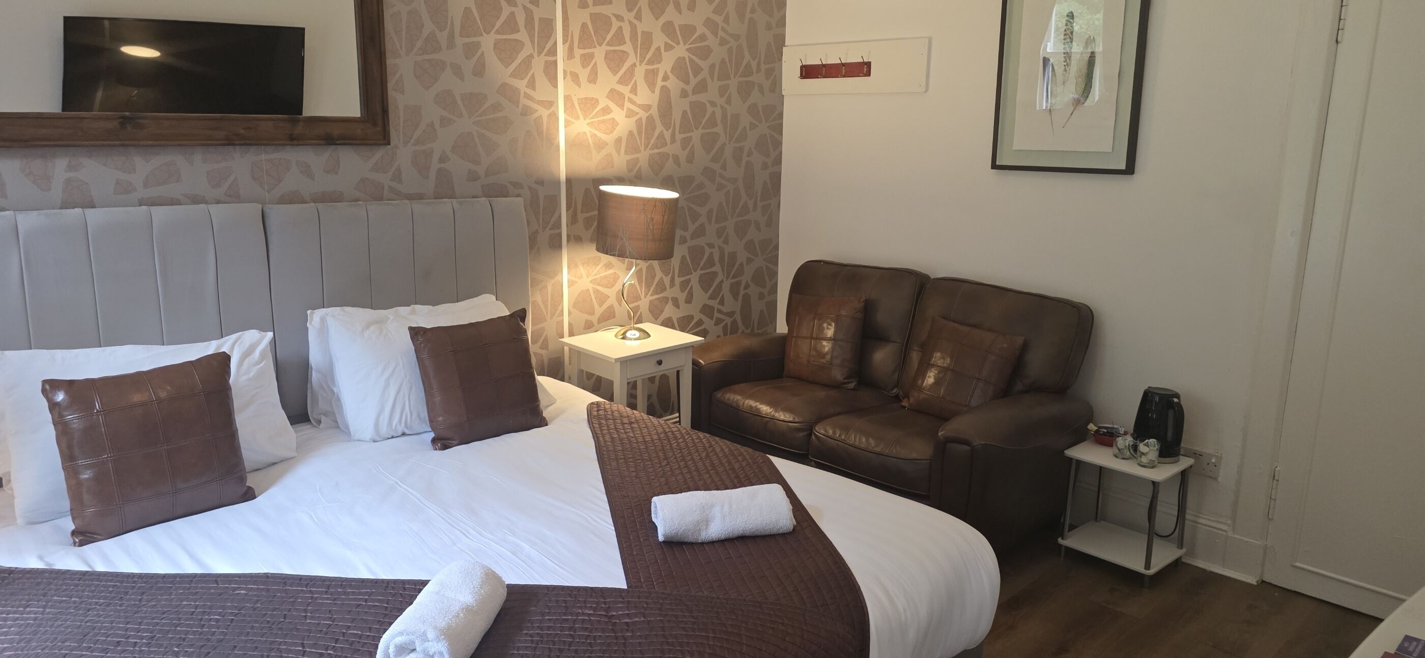 A hotel room with a large bed, a leather sofa, a bedside table with a lamp, and a framed picture on the wall.