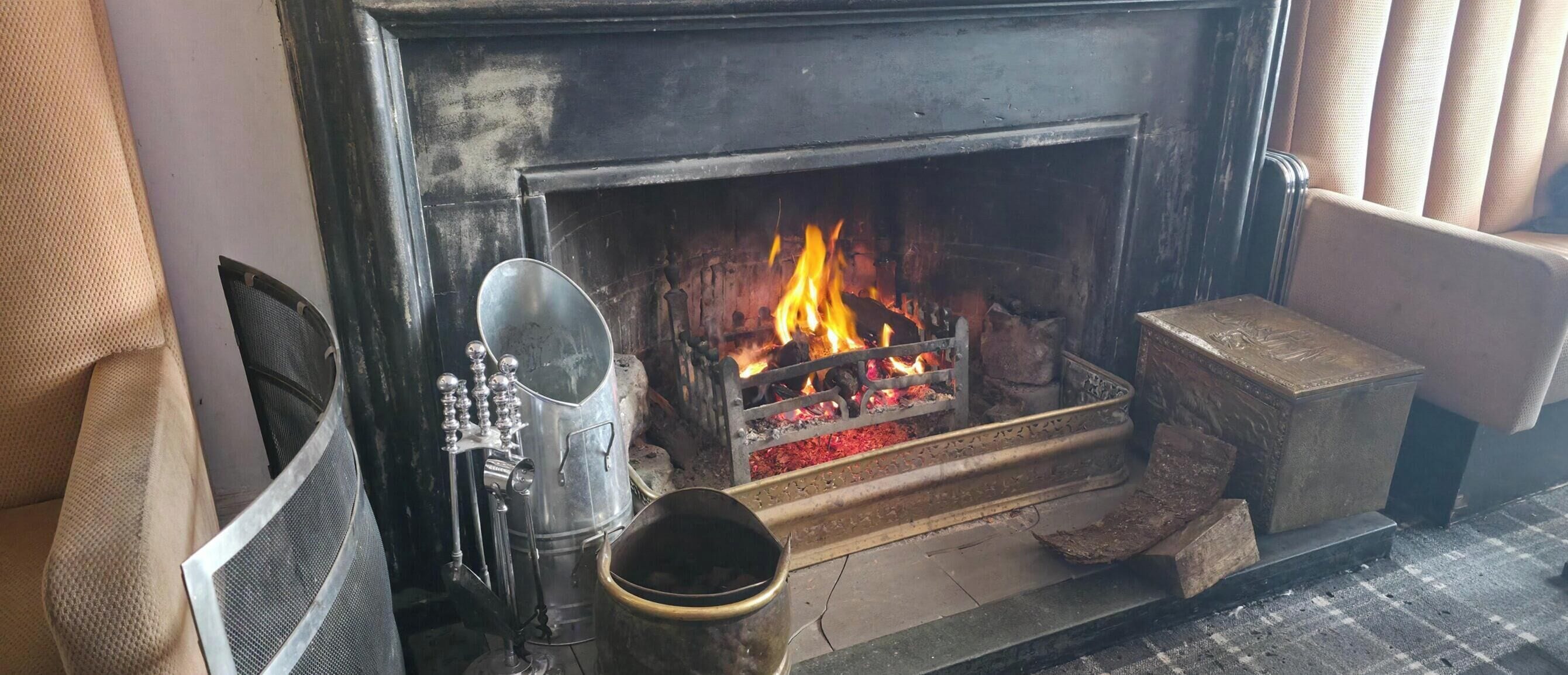 Una chimenea con fuego, una rejilla de metal y un soporte metálico decorativo.