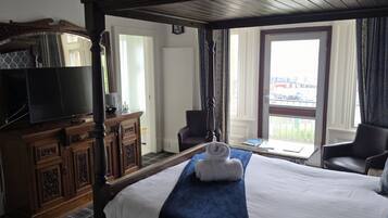A hotel room with a large bed, a television, a desk with a chair, and a view of the outside.