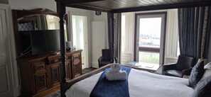 A hotel room with a large bed, a television, a desk with a chair, and a view of the outside. - Royal Marine Hotel (Dunoon)