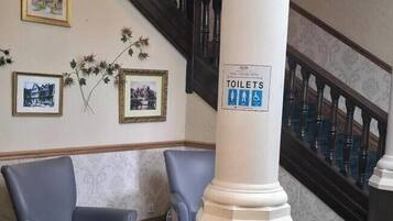 Zona de recepció amb una escala, un senyal indicador de lavabos i dues cadires.