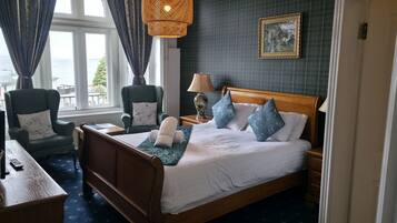 A hotel room with a bed, two chairs, a desk, a lamp, and a painting on the wall.