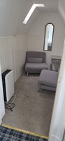 A compact room with a sloped ceiling, a grey sofa, a small bedside table, and a mirror.
