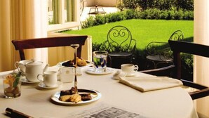 Una mesa dispuesta para una comida, con tazas de té, una tetera, una bandeja de pasteles y un periódico.