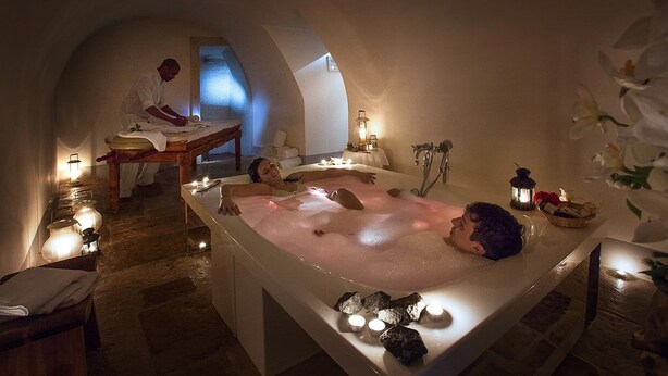Un cuarto de spa con una bañera grande, velas y una camilla de masaje.