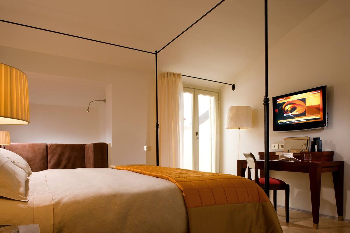 A hotel room with a bed, a desk, a television, and a window with curtains.