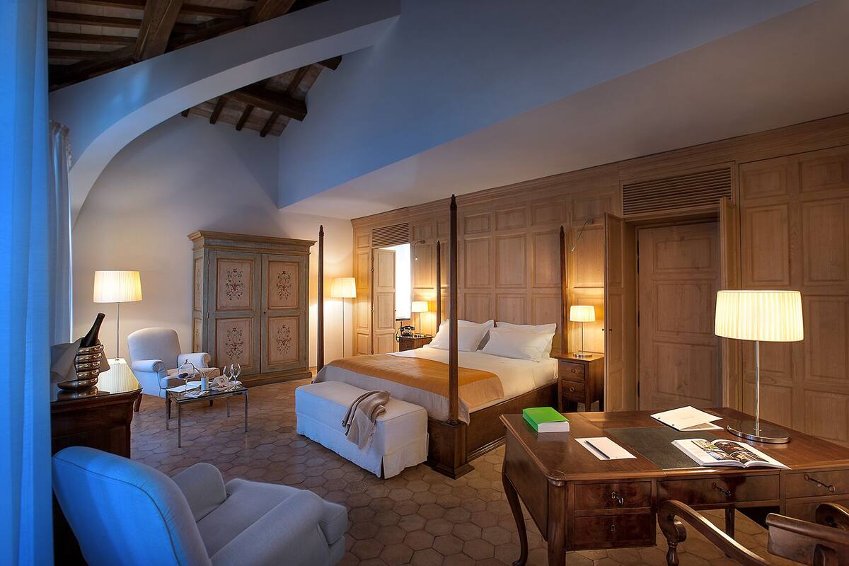 A hotel room with a large bed, a desk, a chair, and a wardrobe.
