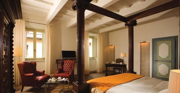 Una habitación de hotel con una cama grande, un sillón rojo, una mesita con lámpara, televisión y un escritorio con lámpara.
