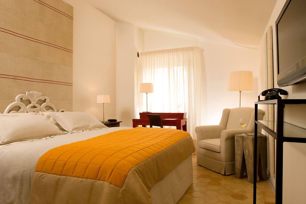 A hotel room with a bed, a desk, a chair, a TV, and a telephone.