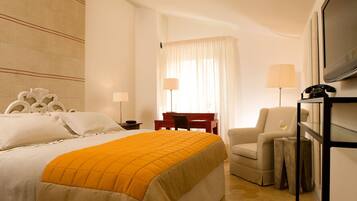 Quarto de hotel com cama, escrivaninha, cadeira, televisão e telefone.