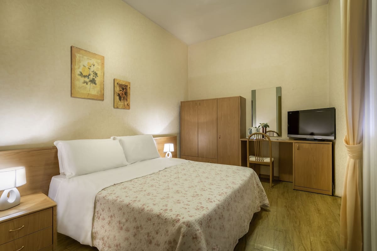 Habitación de hotel con cama, televisión, armario de madera, escritorio y silla, y dos cuadros colgados en la pared.