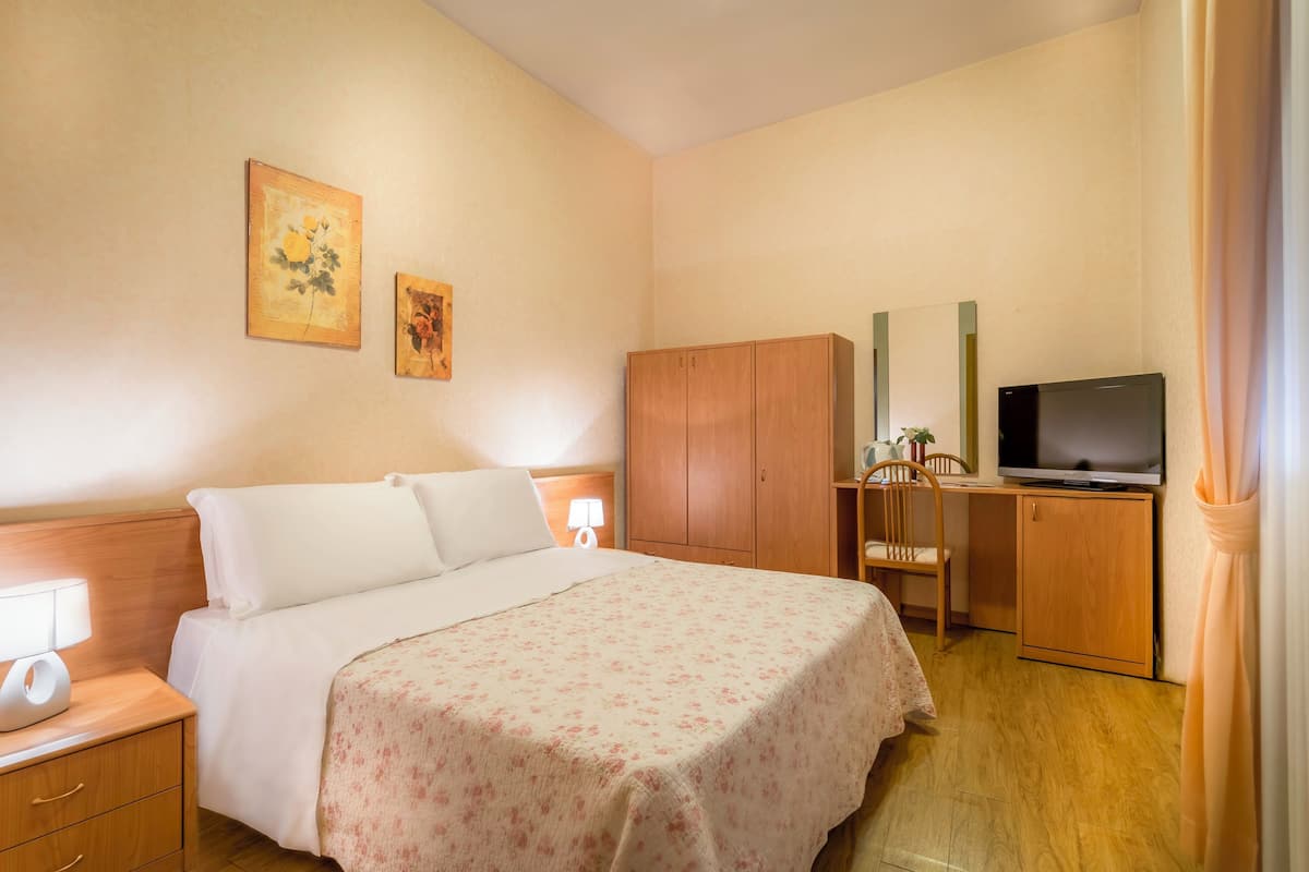 Una habitación de hotel con una cama, un armario de madera, un televisor y un escritorio con una silla.
