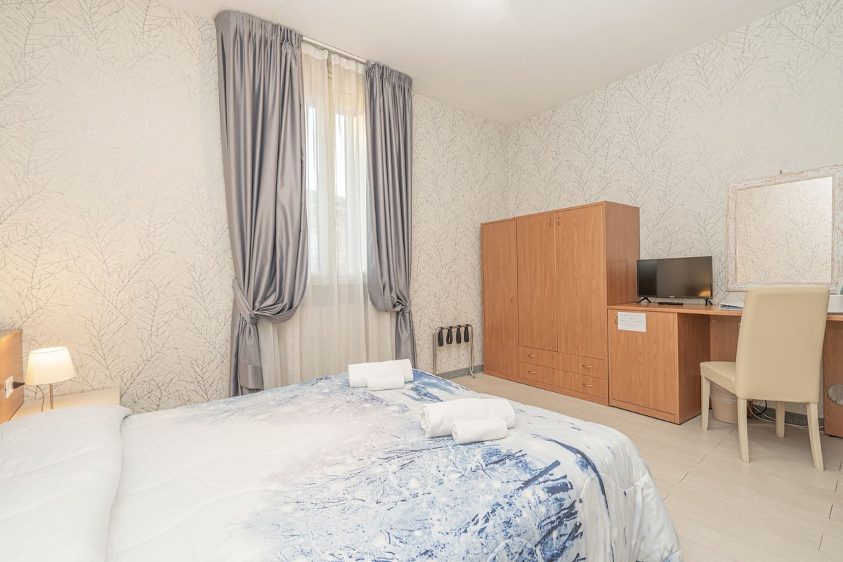 Una habitación de hotel con una cama, un escritorio con ordenador, una silla y un armario.