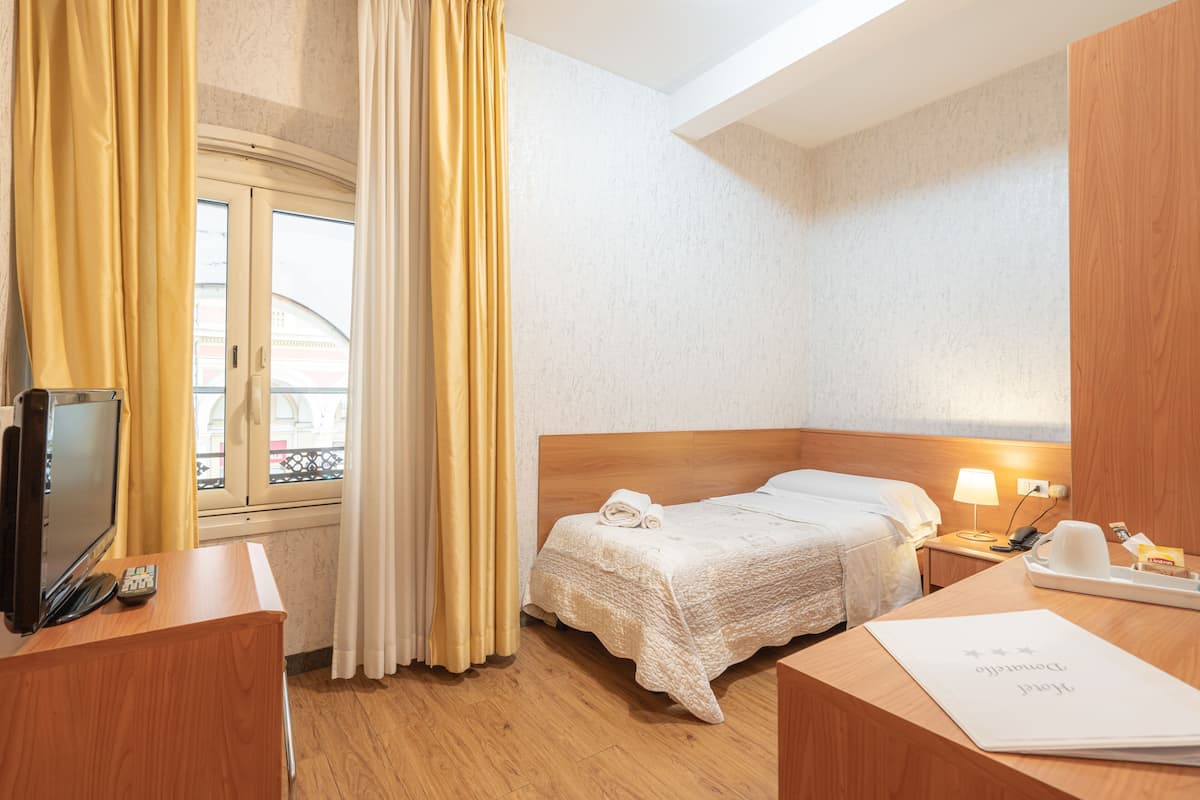Una habitación de hotel con cama, mesita de noche, lámpara y ventana con cortinas.