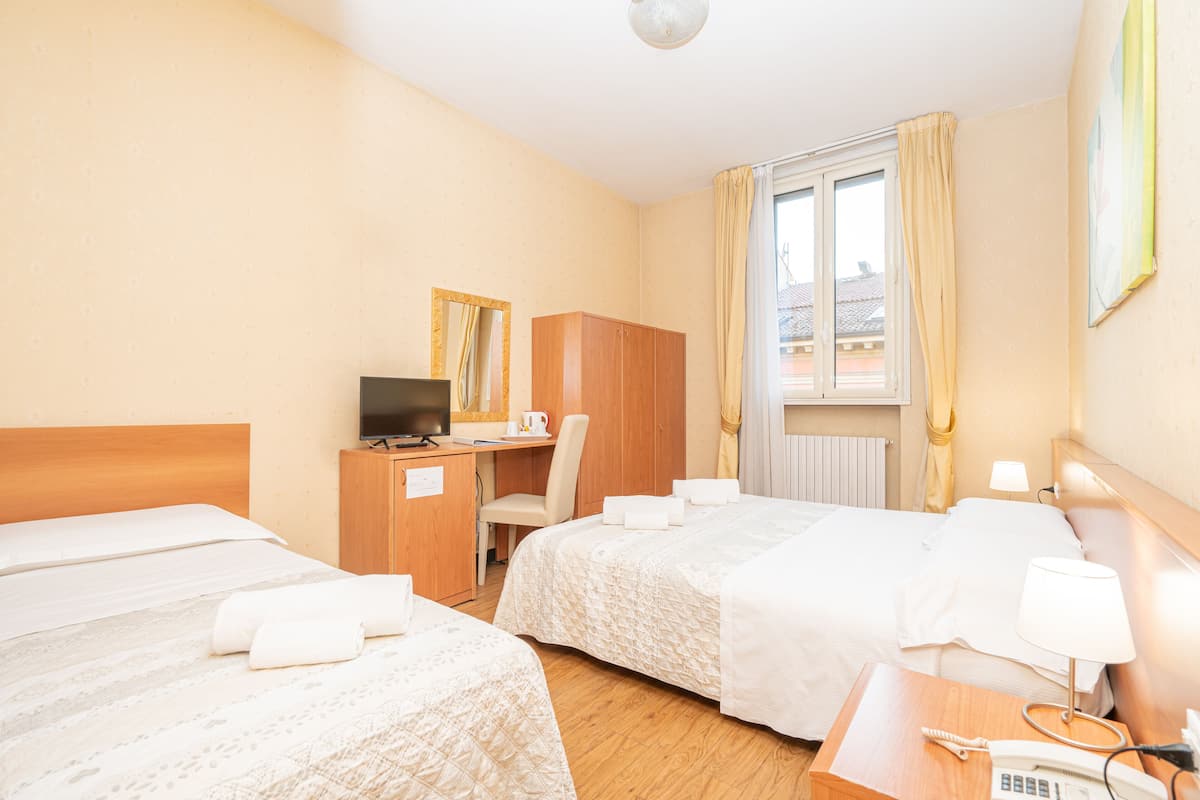 Habitación de hotel con dos camas, un escritorio, una silla, televisión y ventana con cortinas.