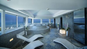 Ein moderner Wellnessbereich mit Whirlpool, Liegestühlen und großen Fenstern mit Blick aufs Meer.