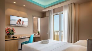 Ein Hotelzimmer mit Bett, Schreibtisch mit Stuhl, Fernseher, Bad und einem Balkon mit Vorhängen.