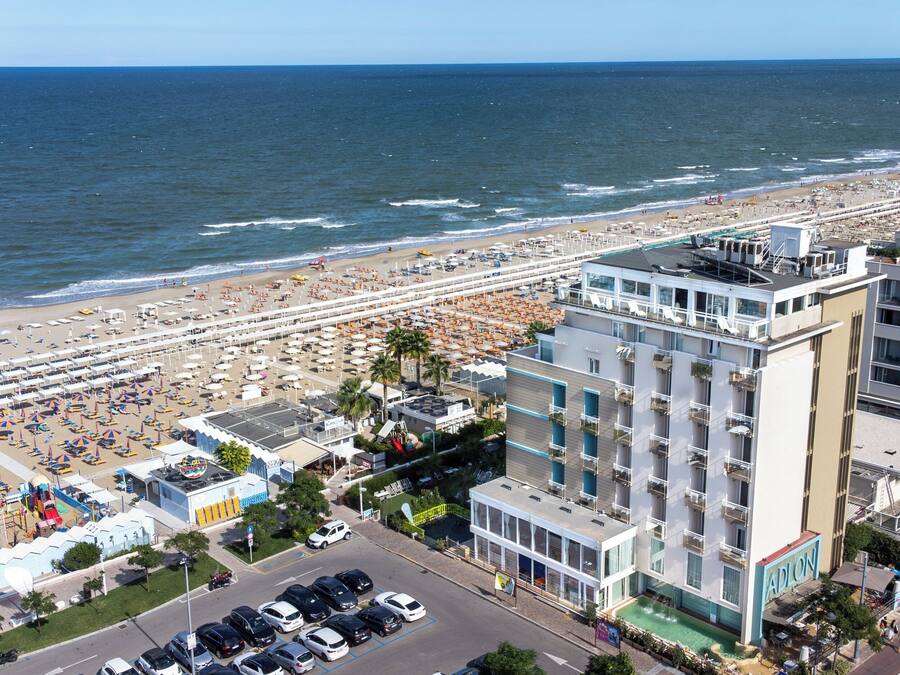 A beachfront hotel with multiple floors, a swimming pool, and a beach area with umbrellas and sun loungers.