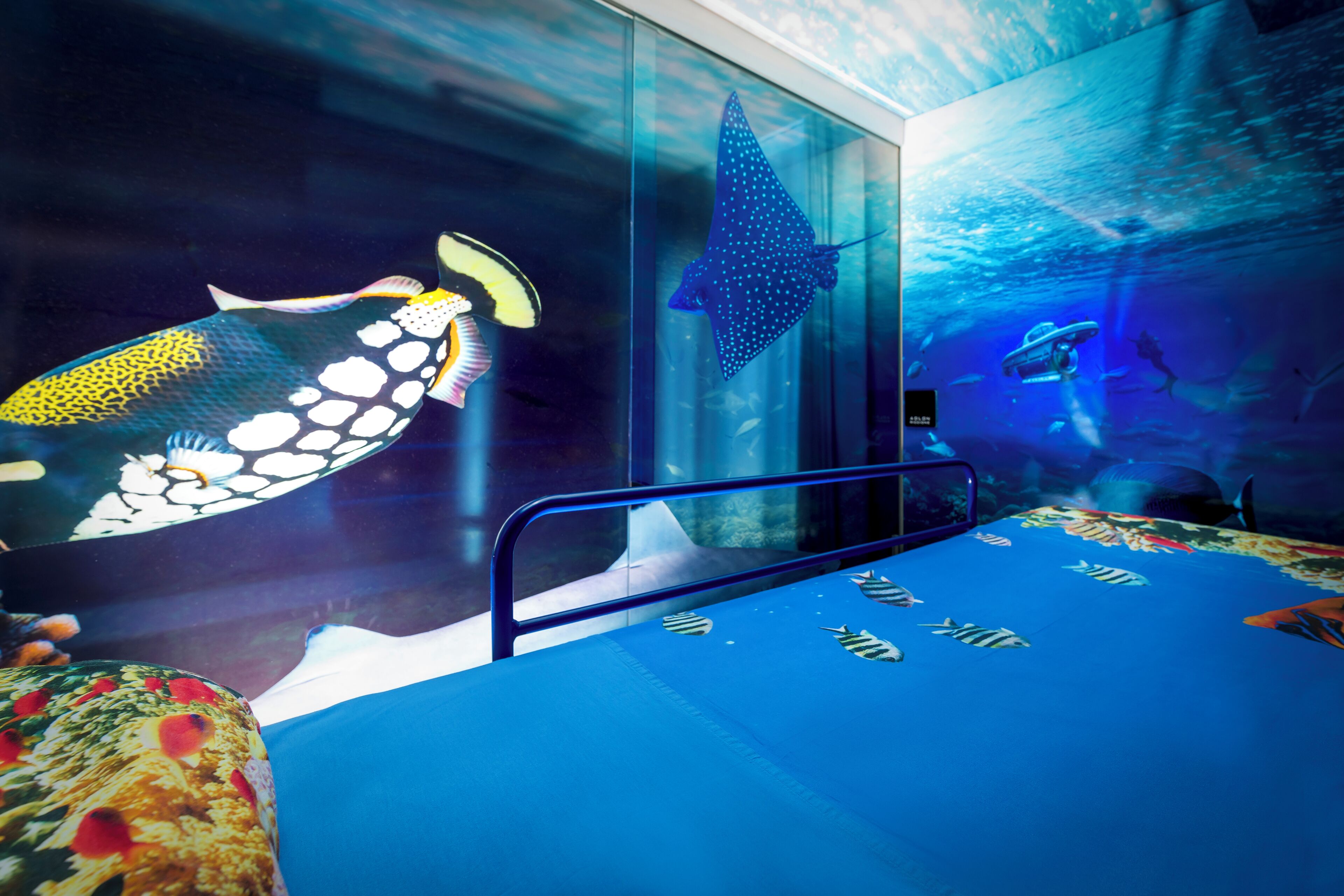 A room with a bed, a glass wall, and a mural of marine life.