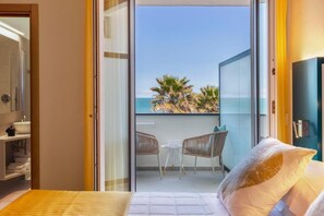 Une chambre d’hôtel avec un lit, une salle de bain et un balcon offrant une vue sur la mer et les palmiers.