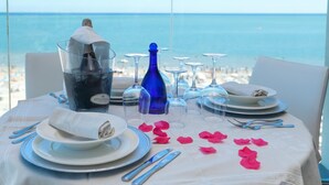 A table set for a meal with a view of the sea, a bottle of champagne, and rose petals on the tablecloth. - Commodore (Riccione)