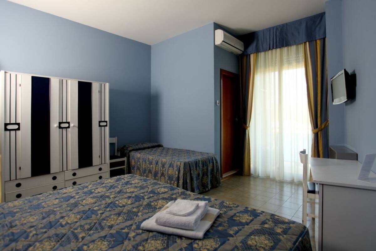 A hotel room with two beds, a wardrobe, a desk, and a TV.