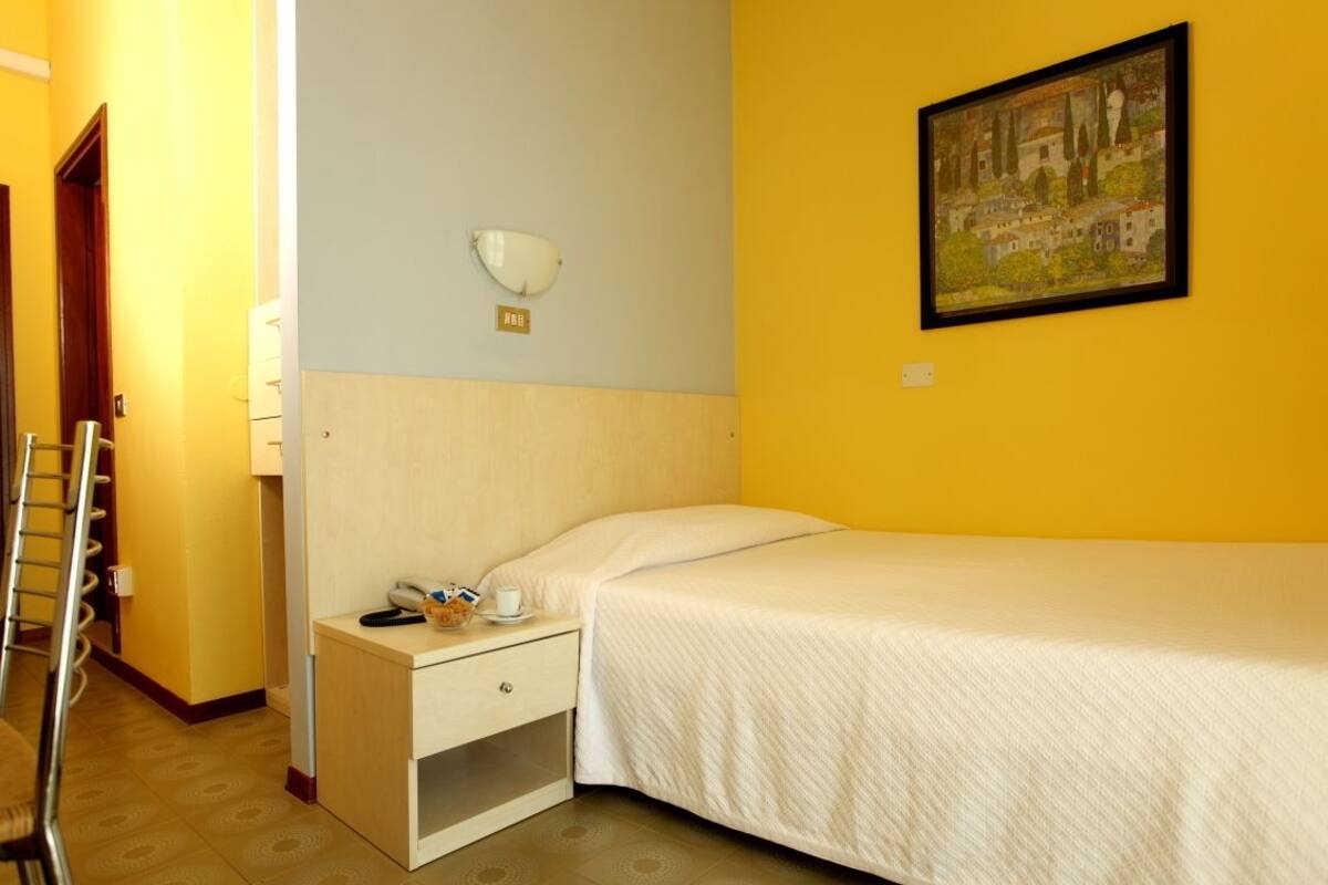 A hotel room with a bed, a nightstand, a lamp, and a painting on the wall.