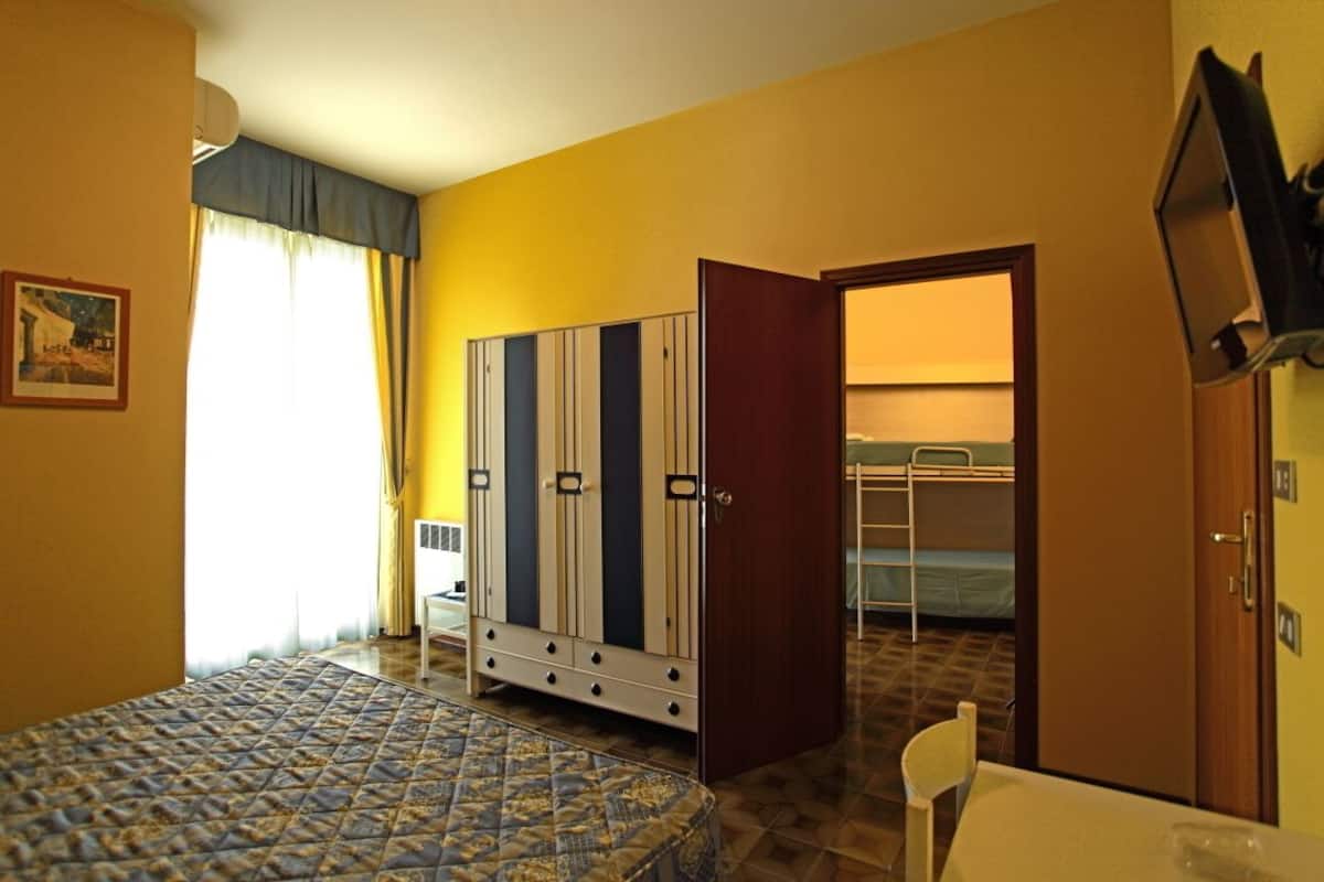 A room with a bed, a wardrobe, a television, and a door leading to a balcony.