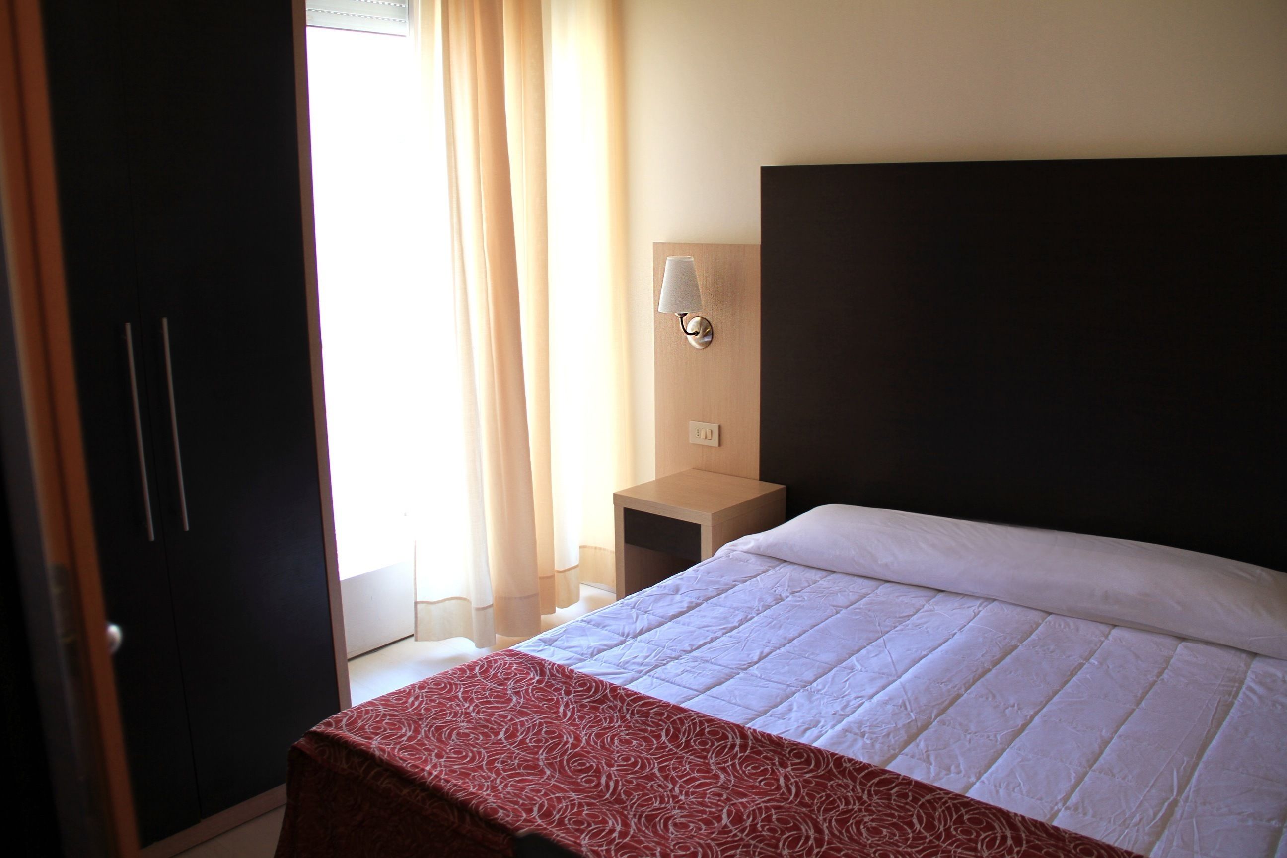 A hotel room with a bed, a nightstand, a lamp, and a wardrobe.