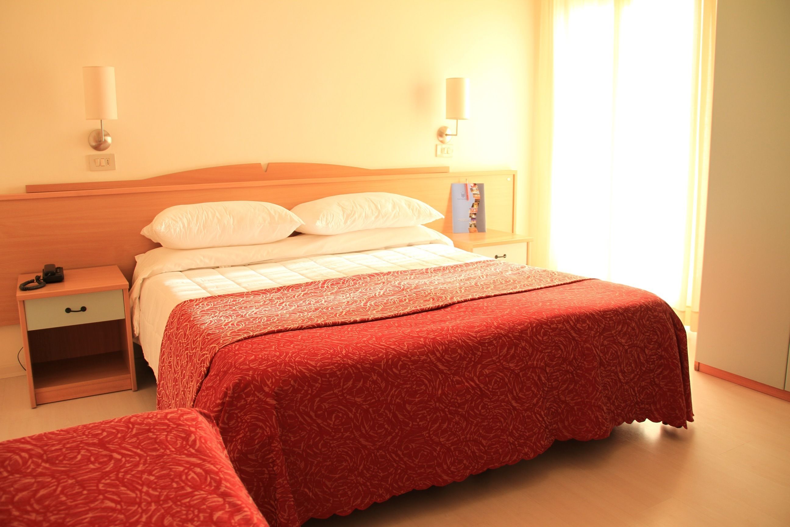 A hotel room with a large bed, a nightstand, a lamp, and a window with curtains.