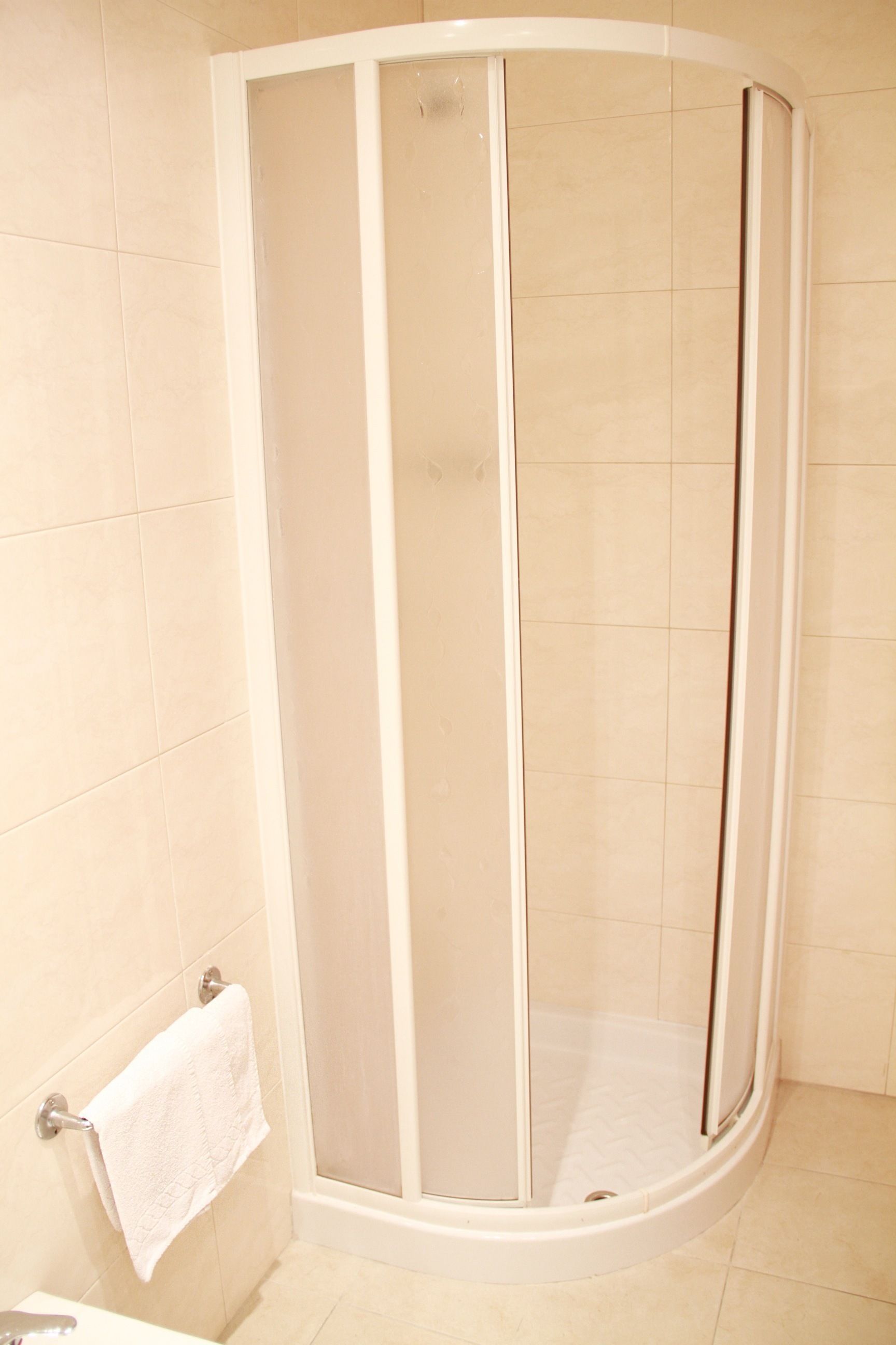 A corner shower enclosure with a glass door and a white towel hanging on a rack.