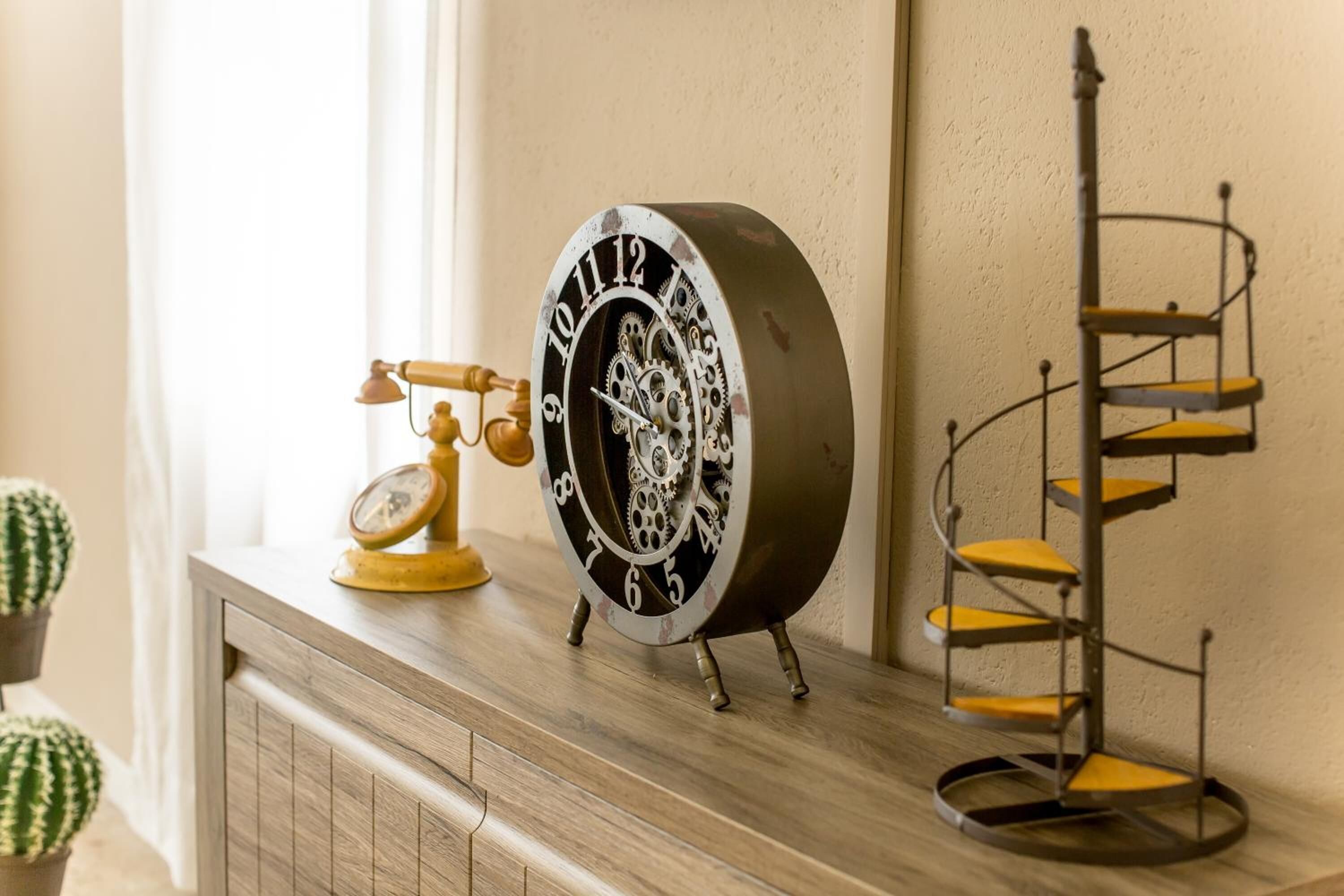 A vintage-style clock with numbers and gears on a wooden surface, next to a metal spiral shelf.