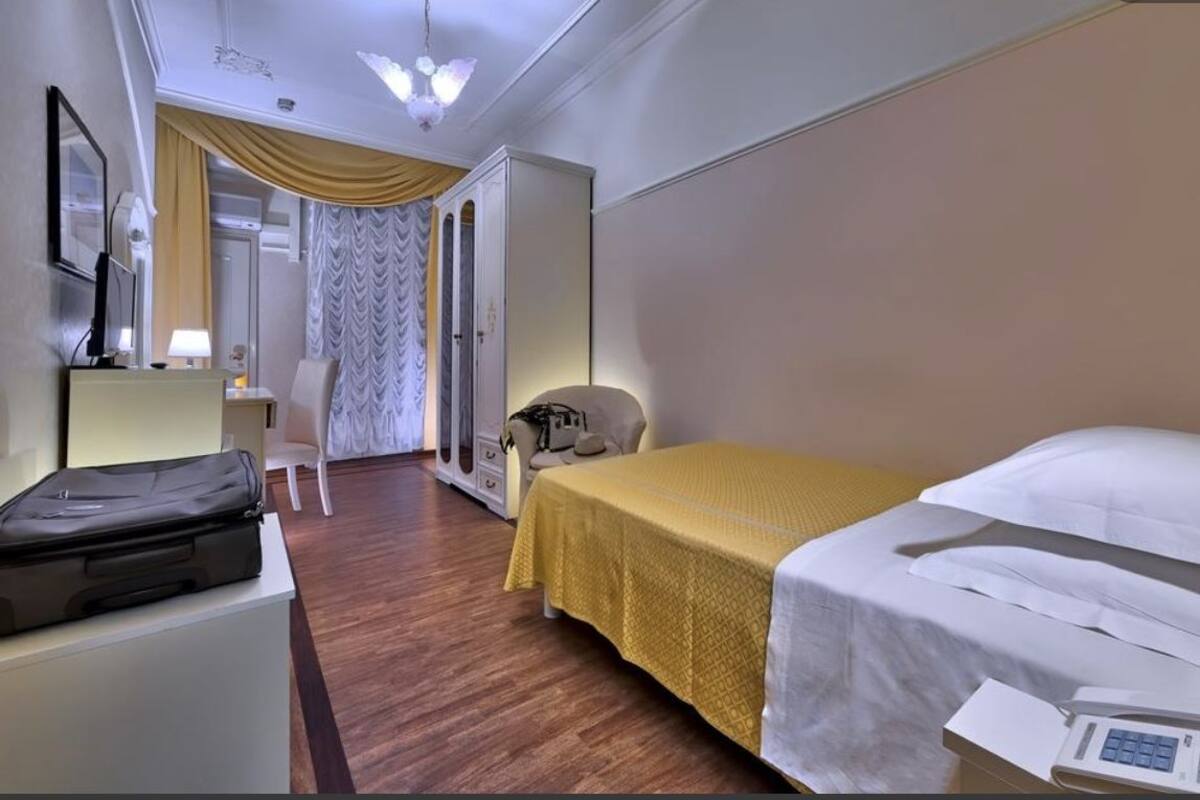 Una habitació d'hotel amb un llit, un escriptori, una cadira, una maleta i una taula de nit amb un telèfon.