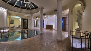 Un hall d’entrée spacieux avec une piscine centrale en verre, des colonnes blanches et une statue.