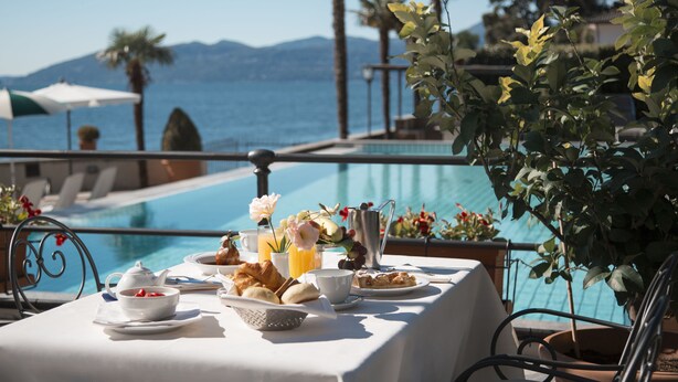 A breakfast table with a view of the sea and mountains, a pool, and some plants. - Hotel Ghiffa (Ghiffa)