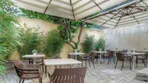 An outdoor patio area with tables and chairs, covered by a canopy, and surrounded by greenery. - Hotel Cosmos (Florence)